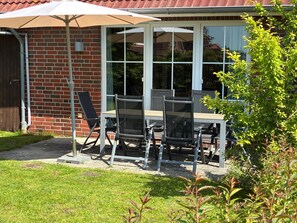 Eine Terrasse mit Tisch und Stühlen, einem weißen Sonnenschirm und einer Backsteinmauer.
