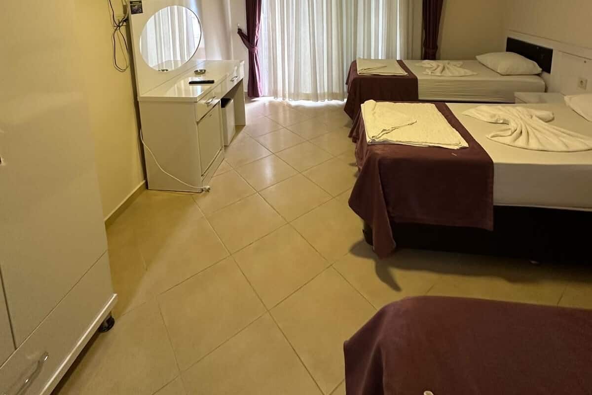 A hotel room with two beds, a desk with a chair, a television mounted on the wall, and a window with curtains.