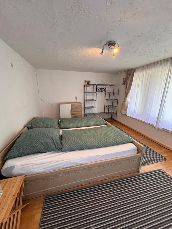 Ein Schlafzimmer mit einem Bett, einer hölzernen Kommode, einem Kleiderschrank und einem Fenster mit Vorhängen.