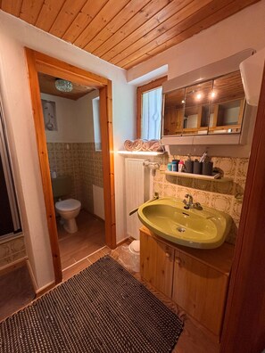 Ein Badezimmer mit Holzwandverkleidung, einem grünen Waschbecken, einer Toilette und einer Duschkabine.