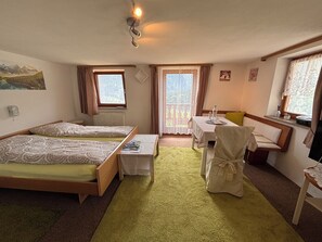 Ein Zimmer mit zwei Einzelbetten, einem kleinen Tisch mit Stuhl, einem Fenster mit Vorhängen und einem Bild an der Wand.