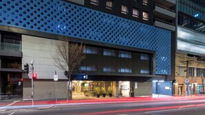 A modern building with a blue perforated facade, a glass entrance, and a visible parking sign. - Exclusive Stays - Gallery Towers (Southbank)