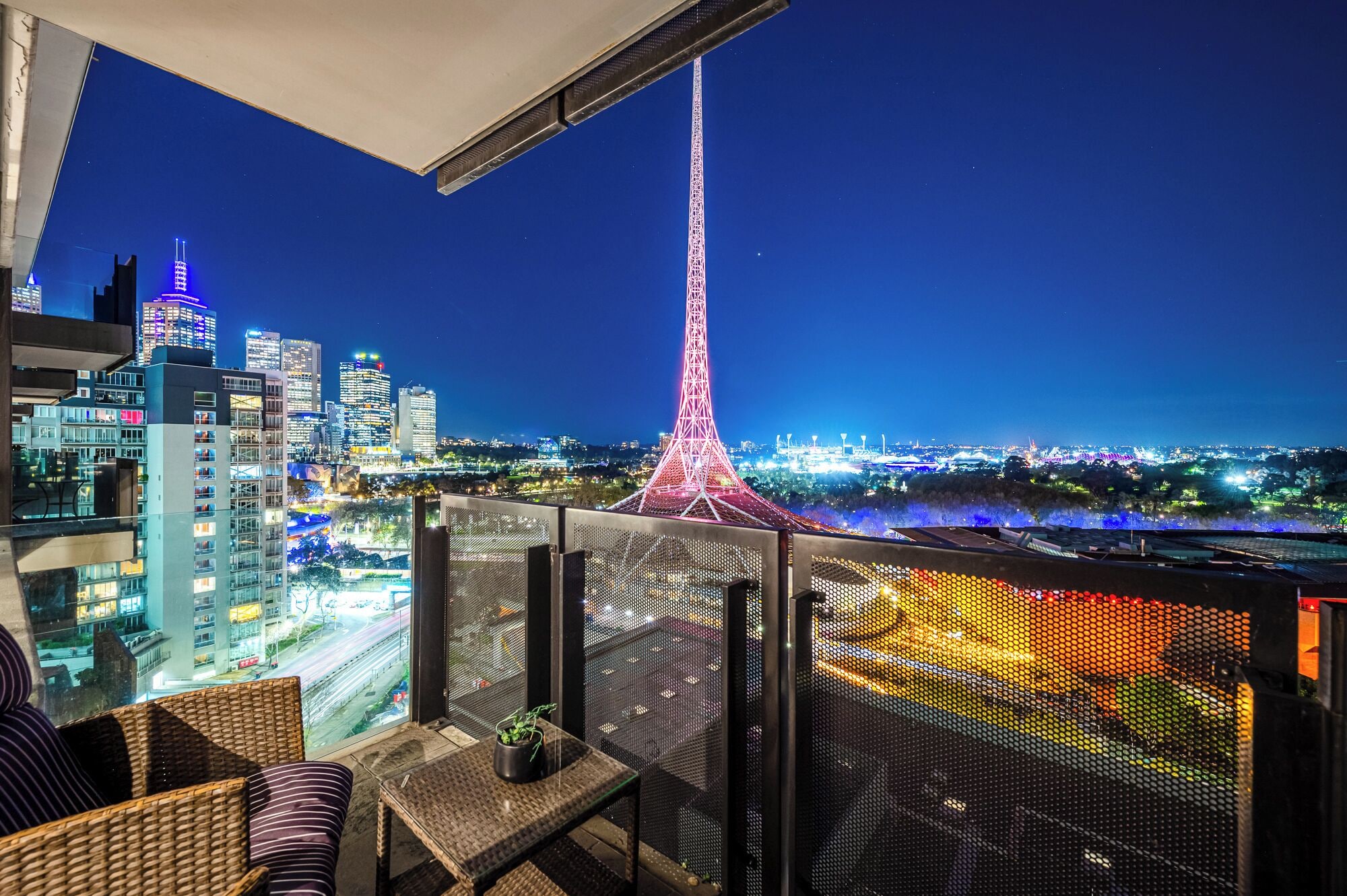 A balcony with a view of a cityscape at night, including a prominent tower and illuminated buildings.