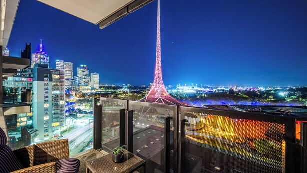 A balcony with a view of a cityscape at night, including a prominent tower and illuminated buildings. - Exclusive Stays - Gallery Towers (Southbank)