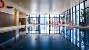 A modern indoor swimming pool with clear glass walls, exit signs, and seating areas. - Exclusive Stays - Gallery Towers (Southbank)