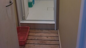 Un pasillo estrecho que conduce a un área de ducha con piso de madera y una cesta roja.