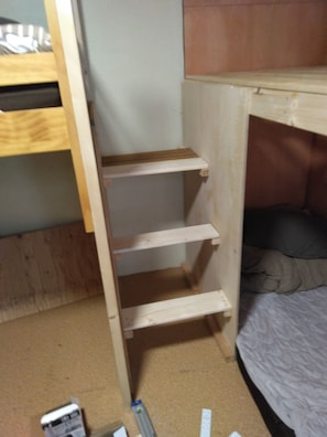 A bunk bed with a wooden ladder, a single shelf, and a small desk area.