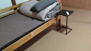 Una cama individual con estructura de madera, una mesita de noche pequeña y un almohadón.