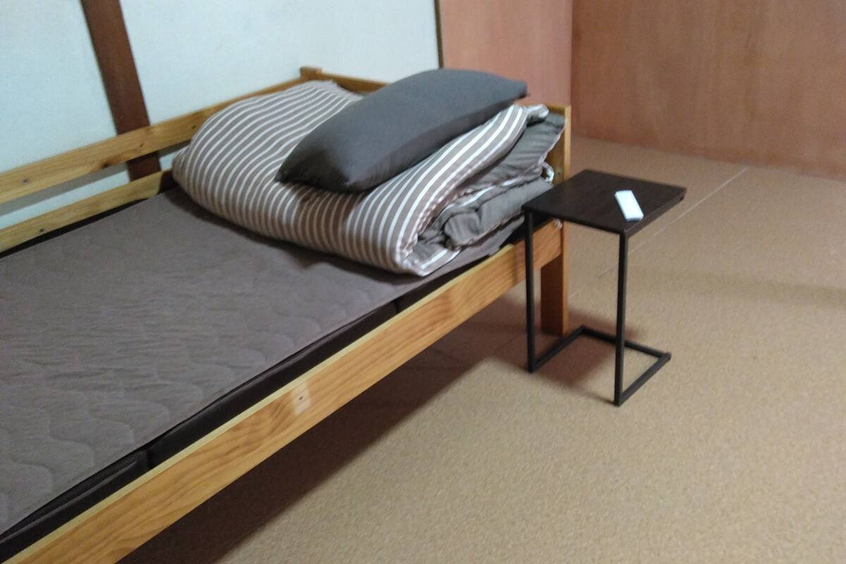 A single bed with a wooden frame, a small bedside table, and a pillow.