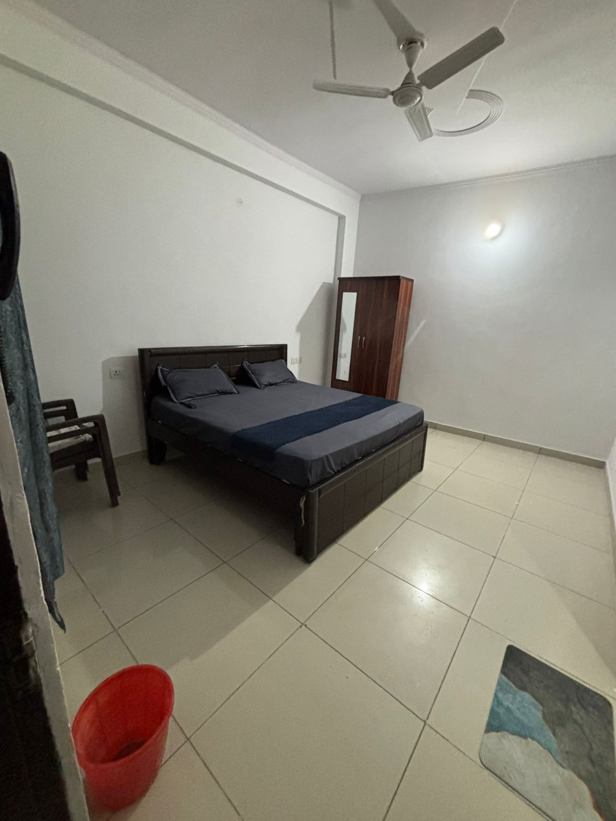Ein Schlafzimmer mit einem Bett, einem Deckenventilator, einem Kleiderschrank und einem roten Eimer auf dem Boden.