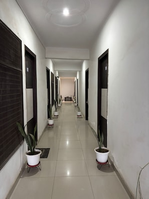 A long, narrow hallway with white walls, black doors, and potted plants. - Hindon Hotel (Ghaziabad)