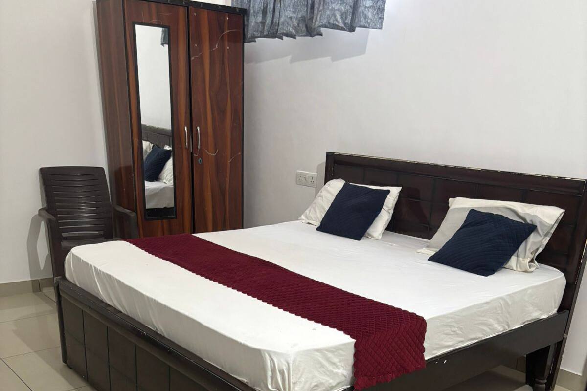 A bed with a wooden frame, a mirror, a wardrobe, and a chair in a room with tiled flooring.