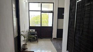 Un pasillo con suelo de baldosas, ventilador de techo, un ventanal y plantas en macetas.