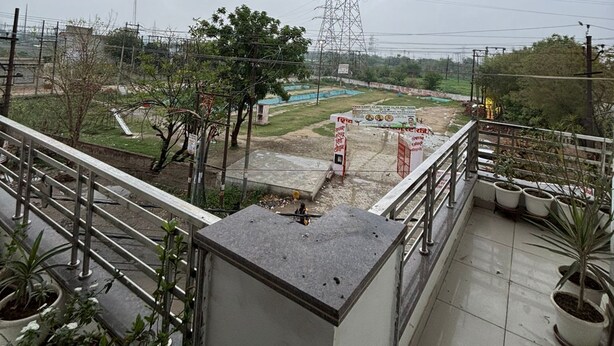 Un balcón con plantas en macetas, vista a una obra en construcción y una torre de tendido eléctrico.