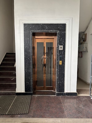 Een gevelingang met een glazen liftingang, een metalen handrail en een trap links.