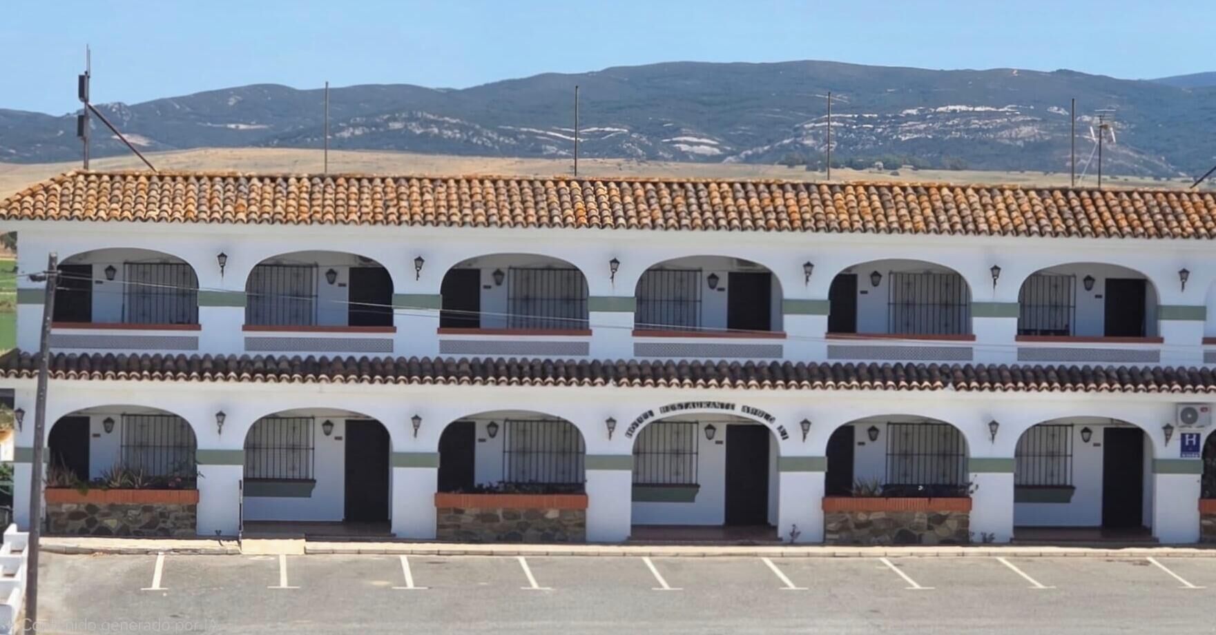 Un edificio a più piani con tetto in tegole, diversi balconi e un parcheggio di fronte.