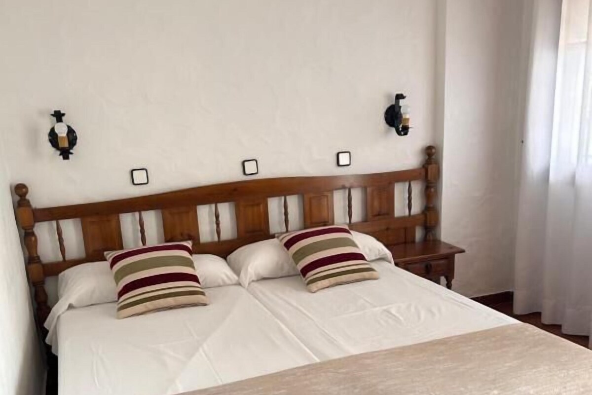 A double bed with a wooden headboard, two bedside tables, and a beige throw blanket.