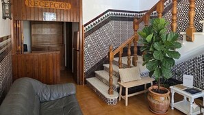 A reception area with a wooden sign, a staircase with patterned tiles, a sofa, and a potted plant. - Hotel Apolo XI (Tarifa)