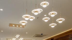 A modern restaurant interior with multiple dining tables, chairs, and hanging pendant lights. - Regenta Place The Golden Castle Baddi (Baddi)