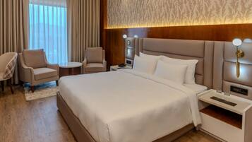 A hotel room with a large bed, two armchairs, a small table, and a nightstand with a lamp.