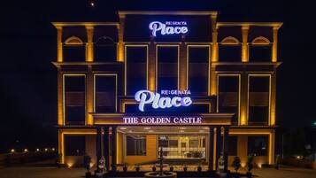Entrada de un hotel con un cartel luminoso que dice 'RE:GEN:TA Place THE GOLDEN CASTLE'.