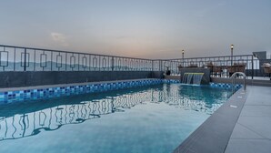 A swimming pool with a tiled edge, a metal fence, and a view of the mountains in the background. - Regenta Place The Golden Castle Baddi (Baddi)