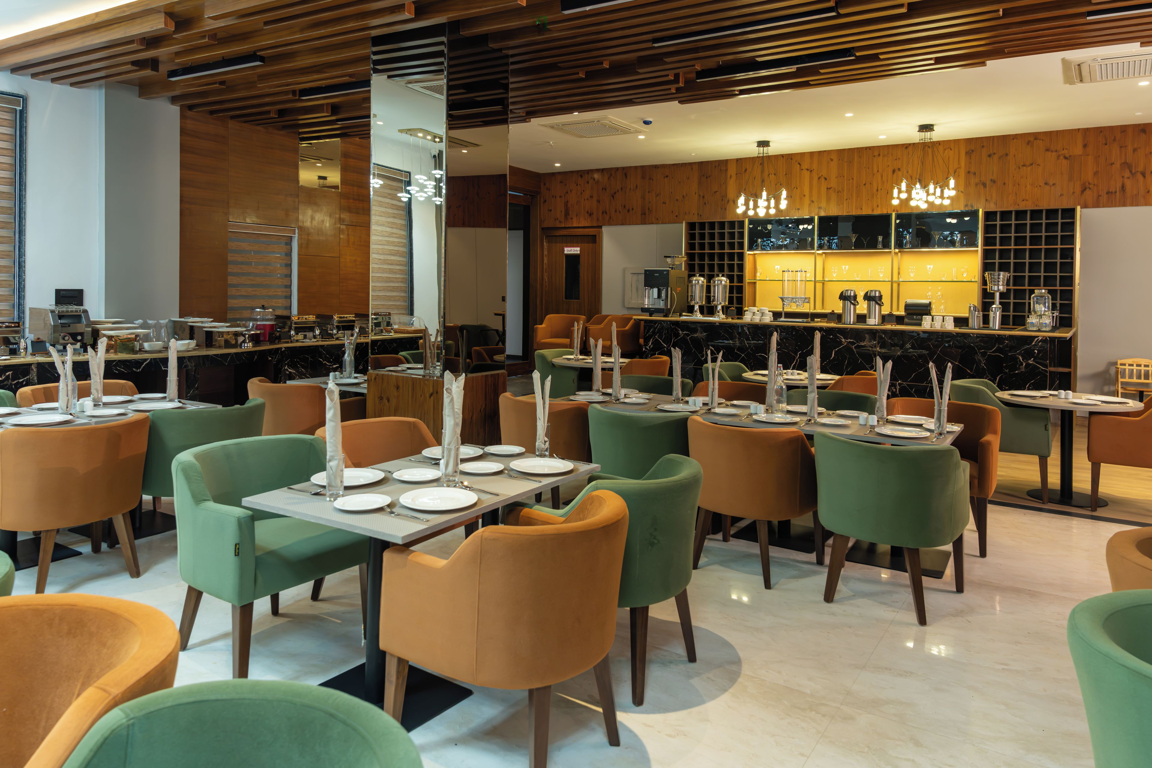A modern restaurant with multiple tables and chairs, a bar area, and a wooden ceiling.