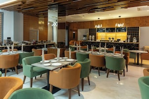 A modern restaurant with multiple tables and chairs, a bar area, and a wooden ceiling.