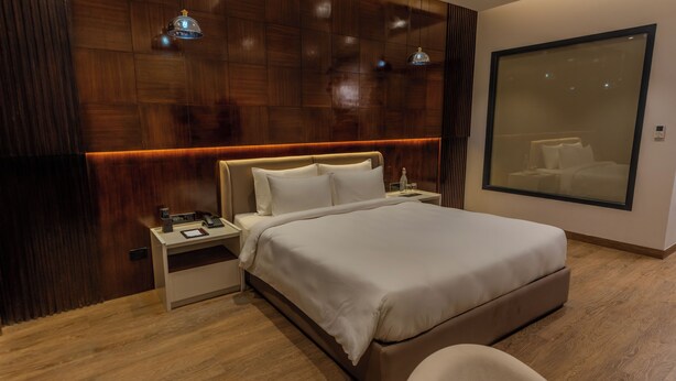 A modern hotel room with a large bed, bedside tables, a nightstand, a chair, and a large window. - Regenta Place The Golden Castle Baddi (Baddi)