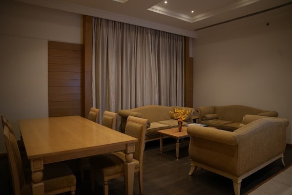 A room with a wooden dining table, two sofas, a small coffee table, and a curtain. - Regenta Place The Golden Castle Baddi (Baddi)