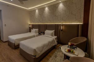 Habitación de hotel con dos camas, una pequeña zona de estar con una mesa y una pared con diseño de mármol.