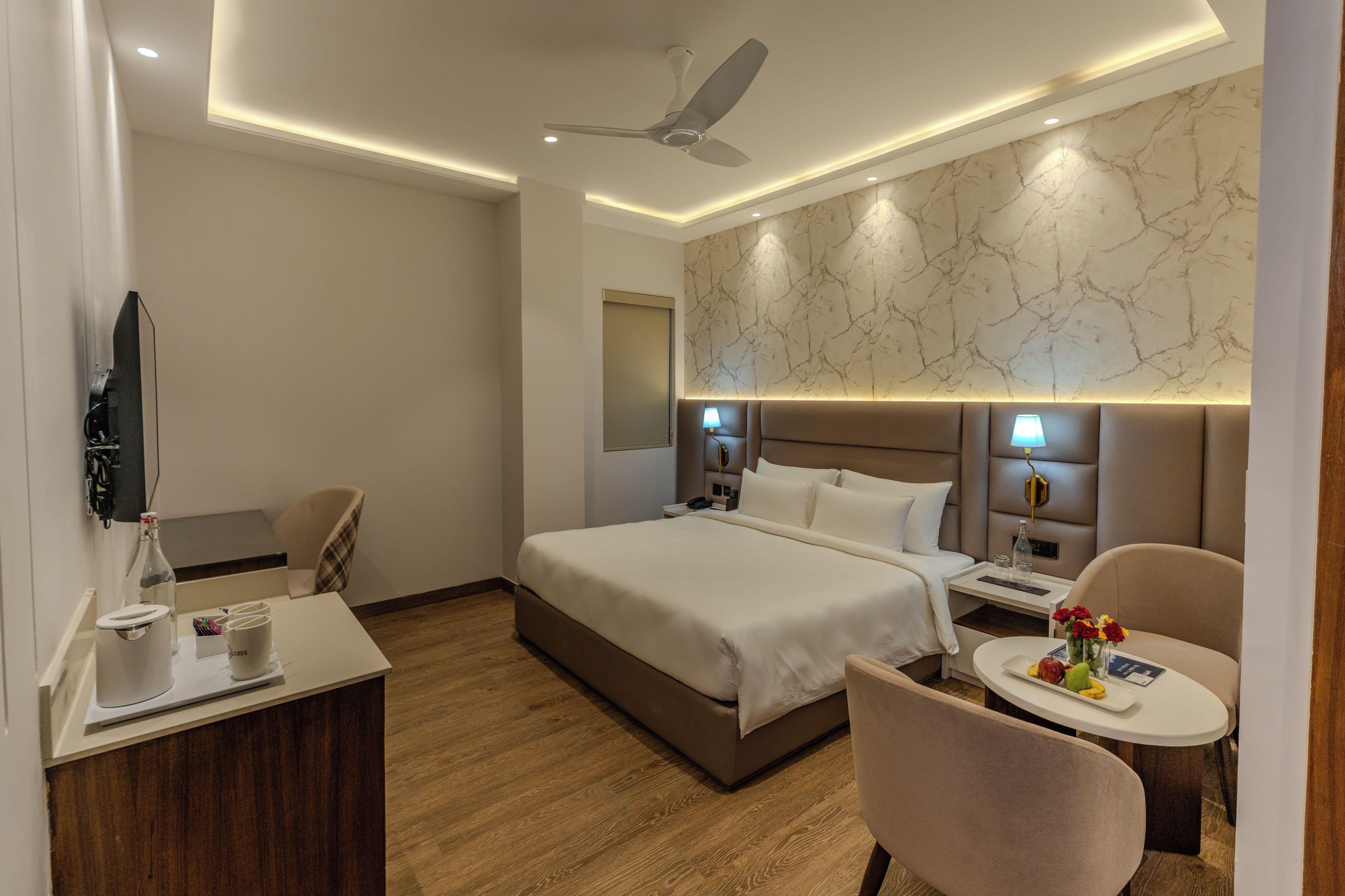 A hotel room with a bed, bedside tables, a desk, a chair, a ceiling fan, and a marble-patterned wall.