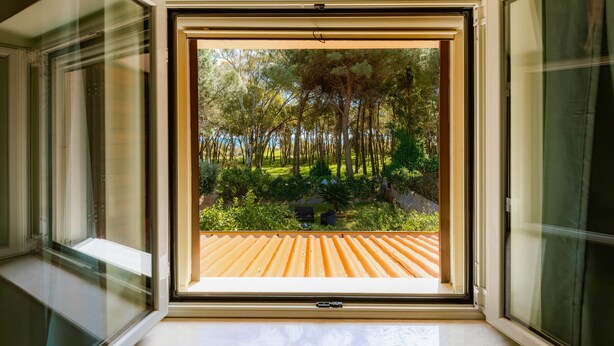 Janela aberta com vista para um jardim e um deck de madeira.