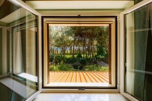 Une fenêtre ouverte donnant sur un jardin et une terrasse en bois.