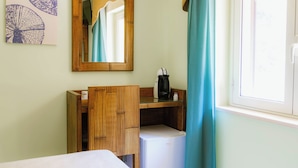 Quarto de hotel com cama, guarda-roupa de madeira, pequena geladeira, cafeteira, espelho e janela com cortinas.