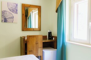 Une chambre d’hôtel comprenant un lit, une armoire en bois, un petit réfrigérateur, une machine à café, un miroir et une fenêtre avec des rideaux.