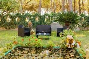 An outdoor seating area with wicker furniture, a small table, and a water feature surrounded by greenery.