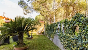 Um jardim com palmeira, parede coberta de hera e um prédio com telhado vermelho.