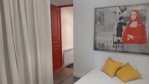 A bedroom with a bed, two pillows, a red door, and a wall-mounted artwork. - Fully-equipped T2 apartment in a country setting close to all amenities, 15 minutes from the beach. (Solliès-Ville)