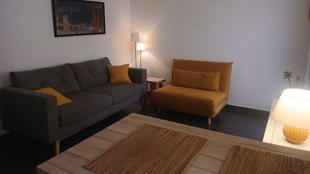 A living room with a sofa, a chair, a coffee table, a lamp, and a framed picture on the wall. - Fully-equipped T2 apartment in a country setting close to all amenities, 15 minutes from the beach. (Solliès-Ville)