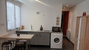 A compact kitchen with a washing machine, a microwave, a sink, and a dining area with stools. - Fully-equipped T2 apartment in a country setting close to all amenities, 15 minutes from the beach. (Solliès-Ville)