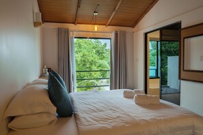 A bedroom with a bed, pillows, a window with curtains, a ceiling light, and a view of greenery outside. - Arena Blanca (Rasdhoo)