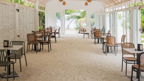 Un espace extérieur abrité, aménagé pour les repas, avec des tables et des chaises, des poutres en bois et des lampes suspendues.