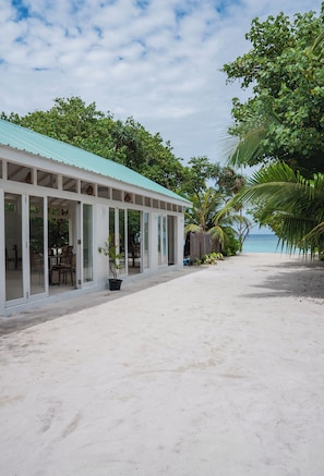 Un edificio frente a la playa con un porche techado, puertas abiertas y vista al océano.