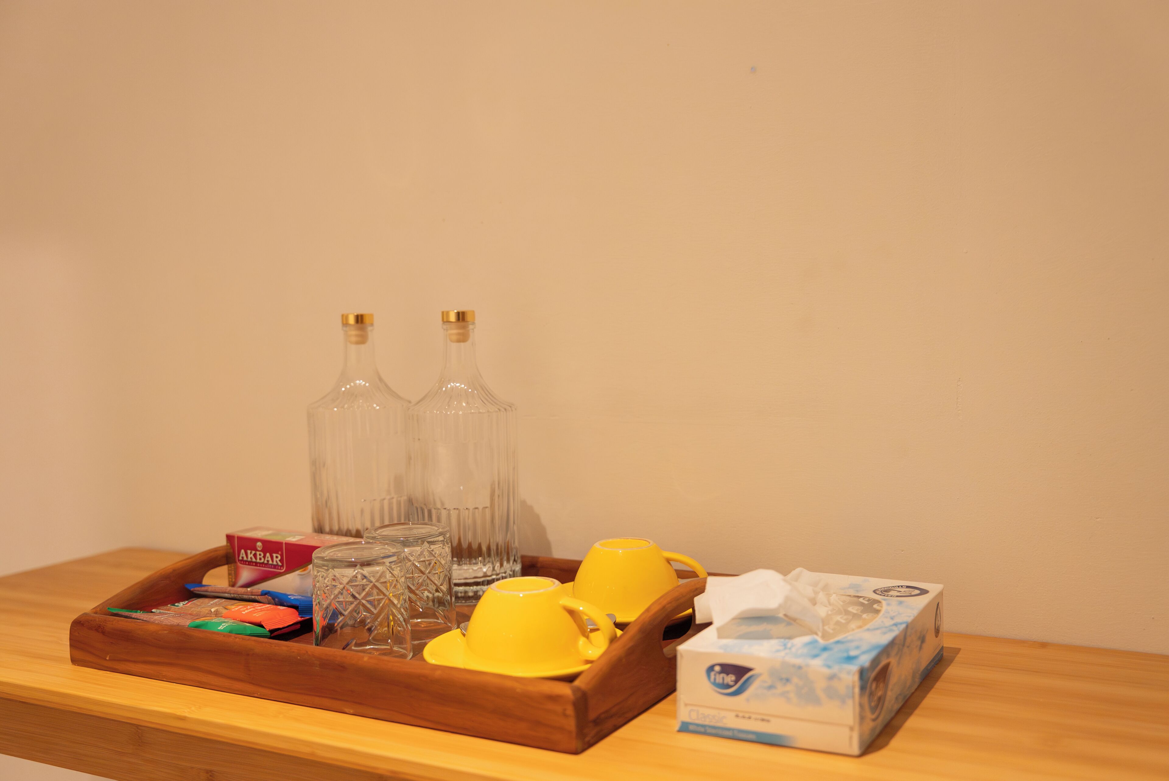 A wooden tray with a tissue box, two yellow cups, a glass, and a box of tissues.