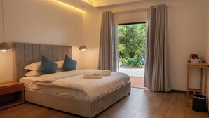 Une chambre moderne avec un grand lit, des lampes de chevet, une table de nuit en bois, une petite table et une vue sur la verdure à l’extérieur.