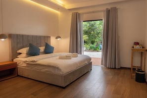 A modern bedroom with a large bed, bedside lamps, a wooden nightstand, a small table, and a view of greenery outside.