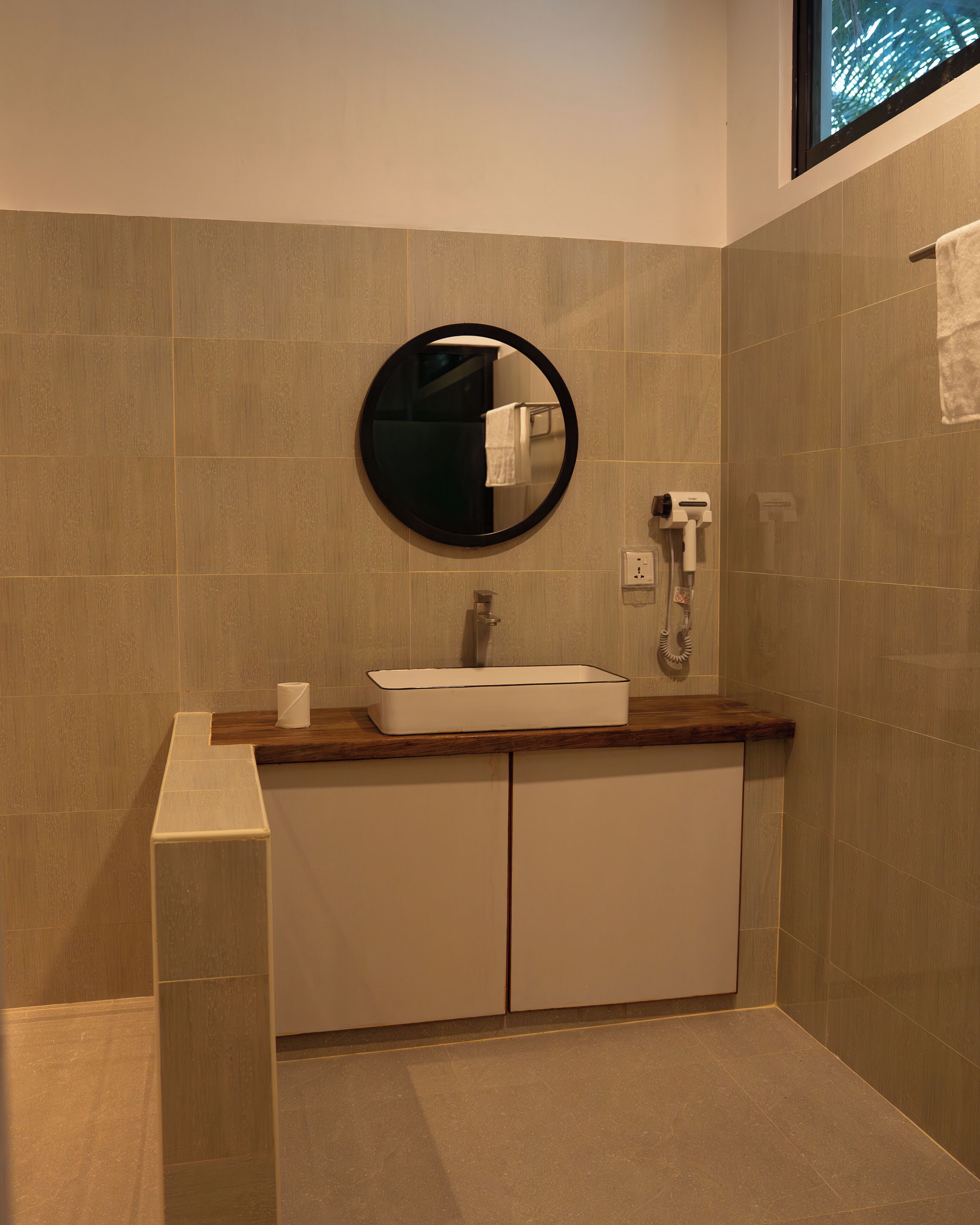 Un baño con un espejo redondo, un lavabo, un perchero para toallas y un secador de pelo.