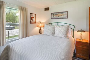 Ein Schlafzimmer mit einem großen Bett, einer Lampe, einem Schminktisch und einem Fenster mit Vorhängen.