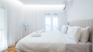Una habitación de hotel moderna con una cama grande, una mesita de noche y una ventana con cortinas traslúcidas.